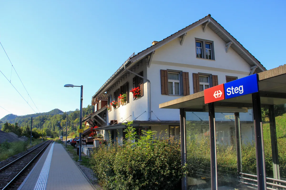 Man sieht ein altes Bahnhofgebäude mit einer neueren Haltestelle daneben.
